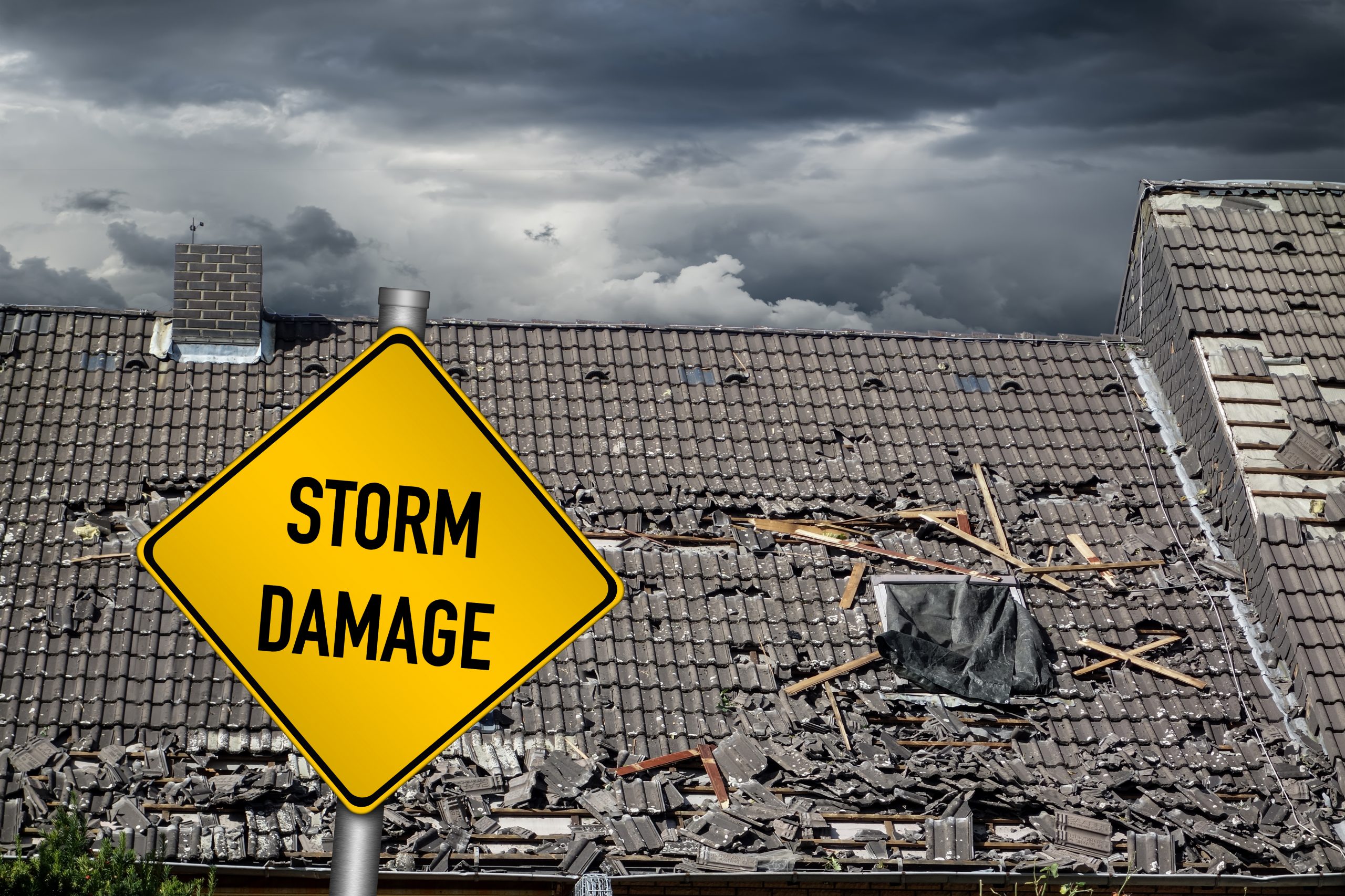 sign reading "storm damage" in front of house with roof damage