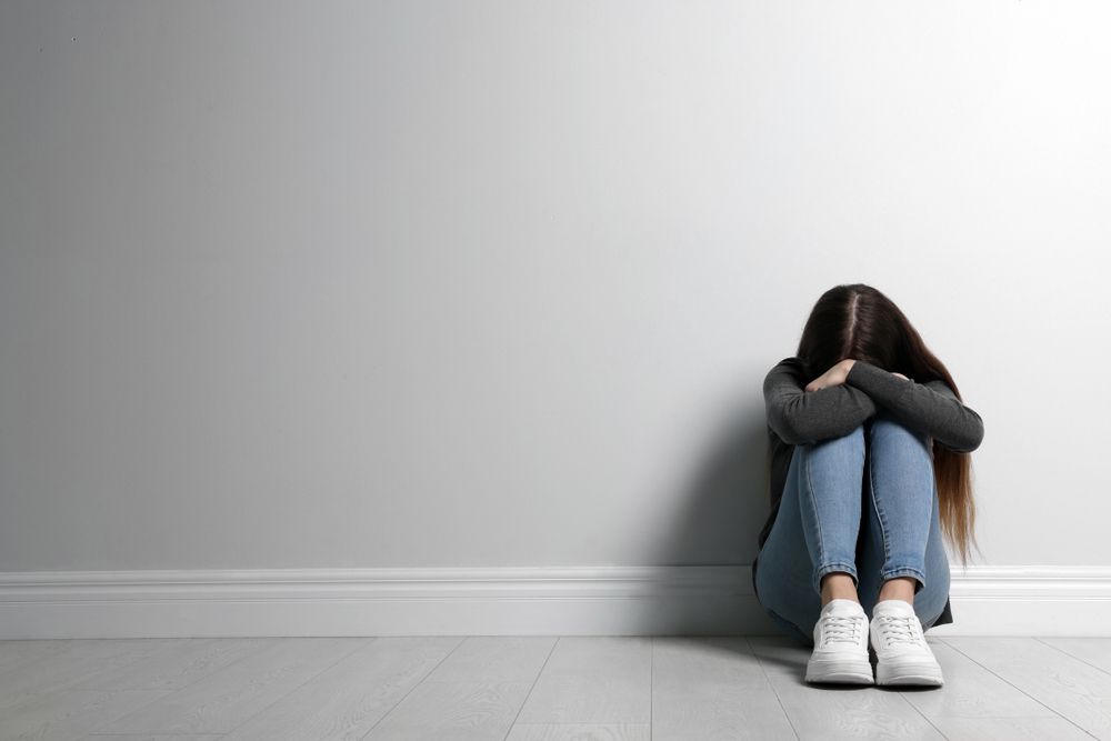 Upset teenage girl sitting on floor near wall.