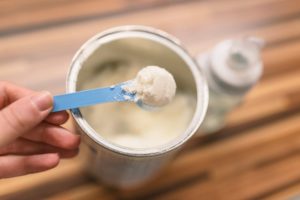 Powder milk and blue spoon on light background close-up.