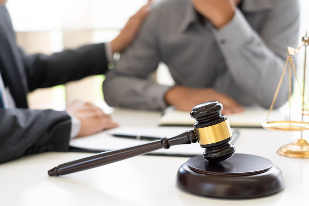 Lawyer putting his hand on the shoulder of a client consoling at desk with a gavel and scales