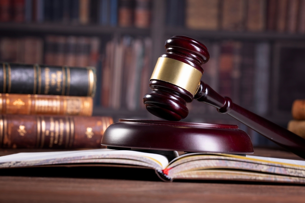 a wooden gavel on a legal book opened on a desk with books behind