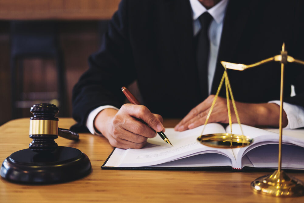 attorney at desk writing a document with a gavel and scales of justice in the foreground