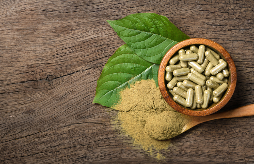 kratom leaves , powder and capsules on a wooden background